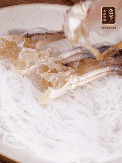 盤底墊上粉絲，擺上梭子蟹、火腿片，撒姜粒，淋上蒸魚豉油、花雕酒調味腌制15分鐘